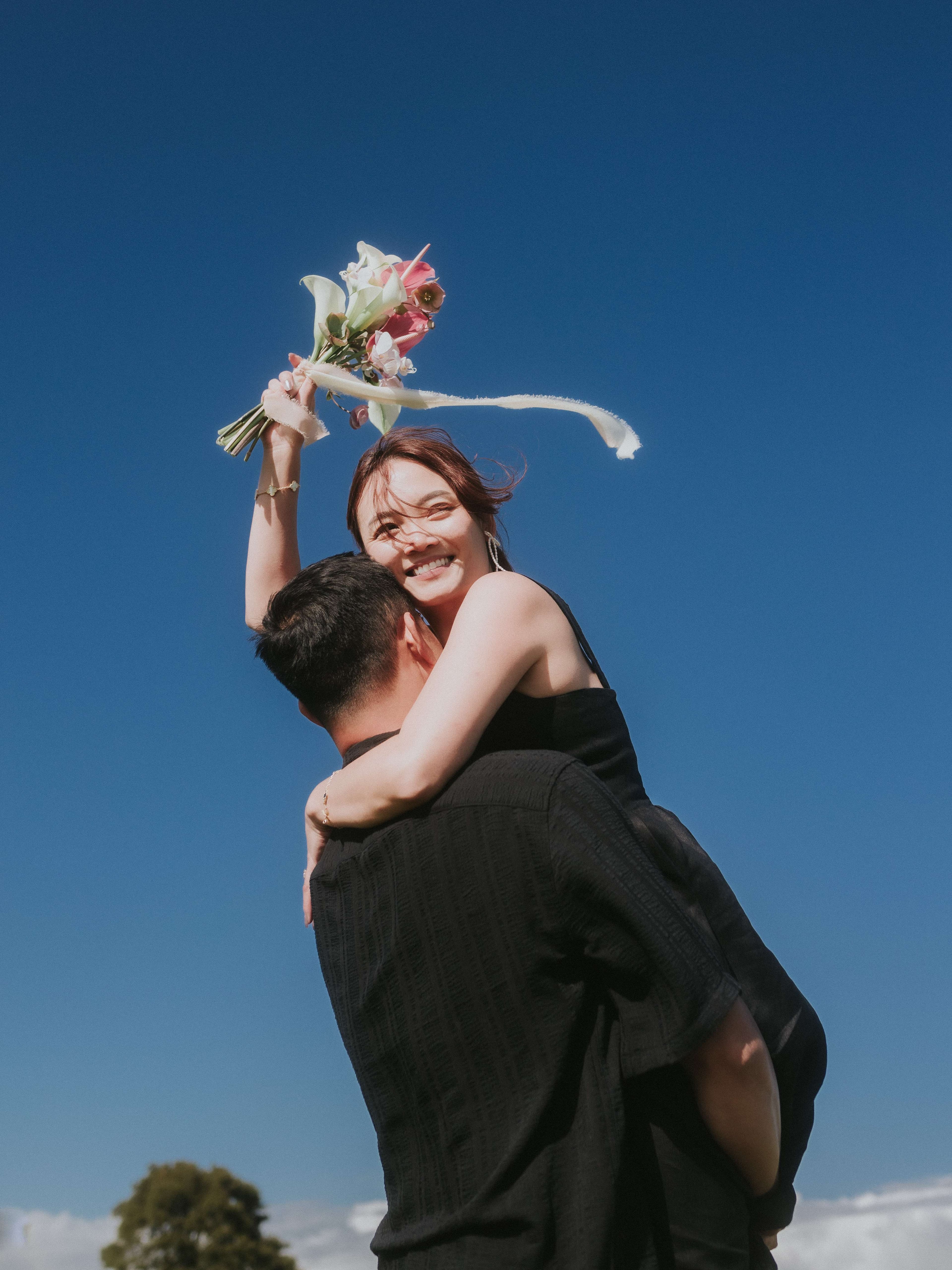Couple celebrating outdoors, the bride holding her bouquet up to a blue sky